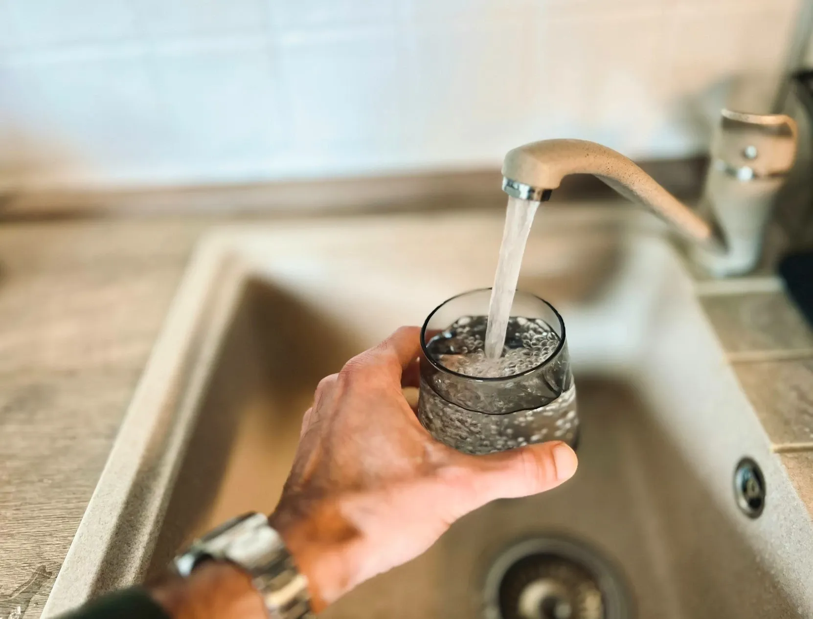 A hand filling a glass with clear tap water from a kitchen faucet in a Medford, Oregon home